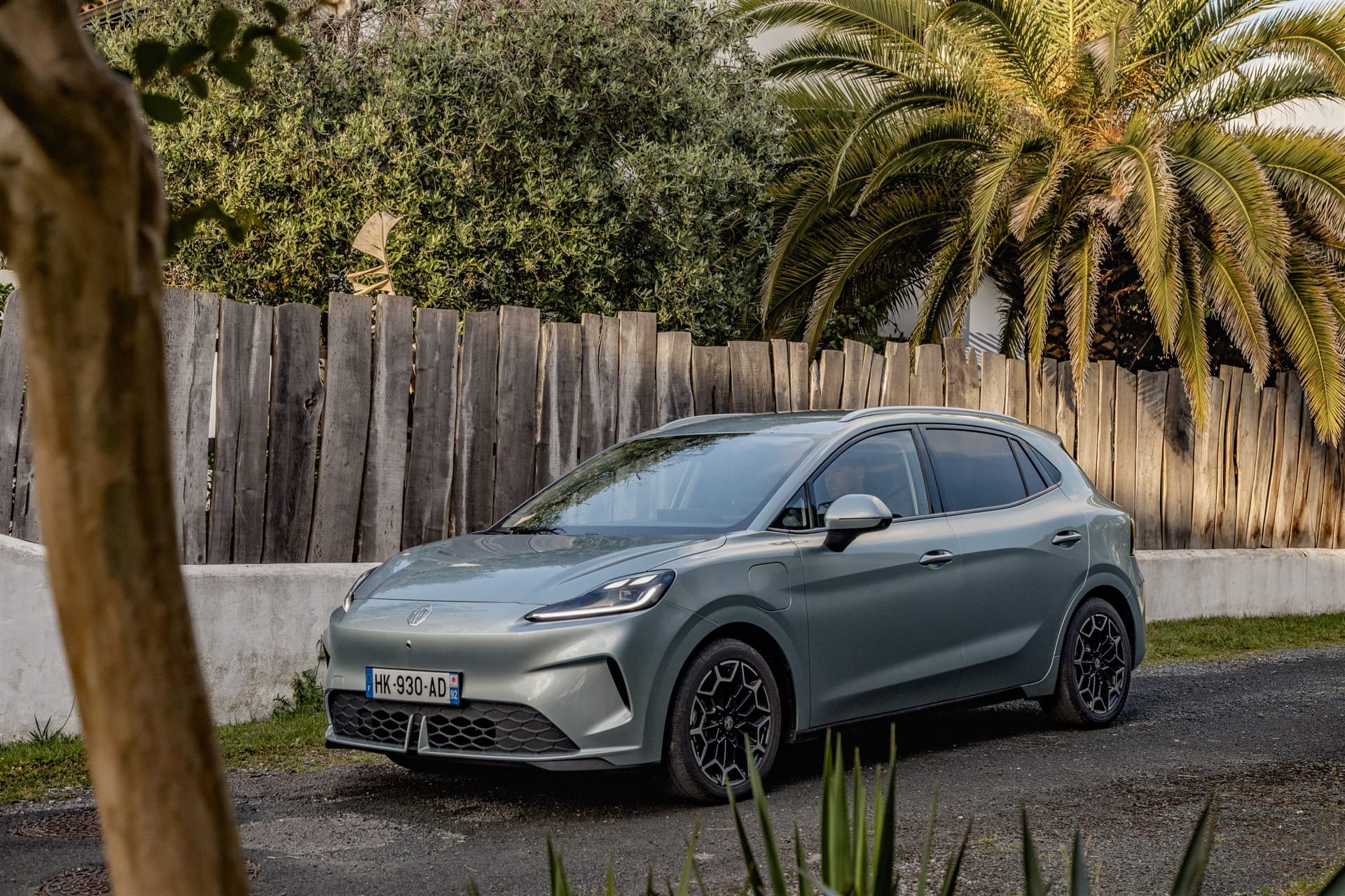 MG4 EV Urban gris stationné devant une clôture en bois et des palmiers