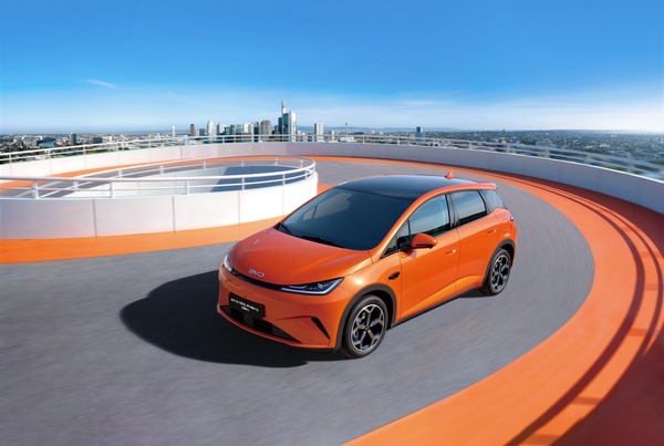 BYD DOLPHIN G DM-i orange roulant sur une piste urbaine avec une ville en arrière-plan