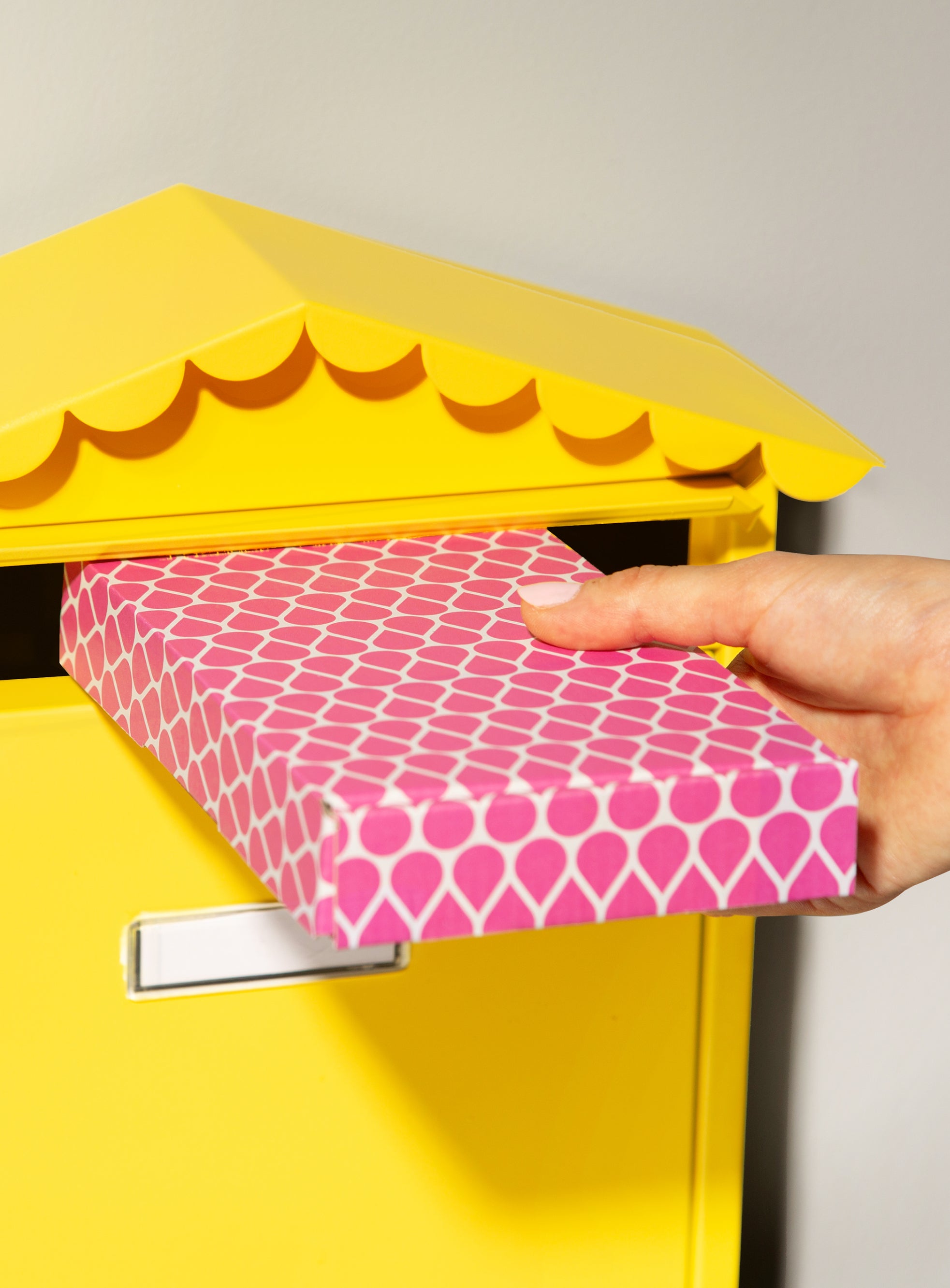 Main deposant un petit colis rose de recharges 900.care dans une boite aux lettres jaune
