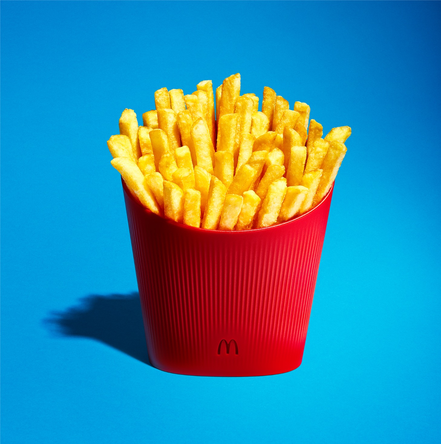 Frites McDonald’s servies dans un contenant rouge réemployable sur fond bleu
